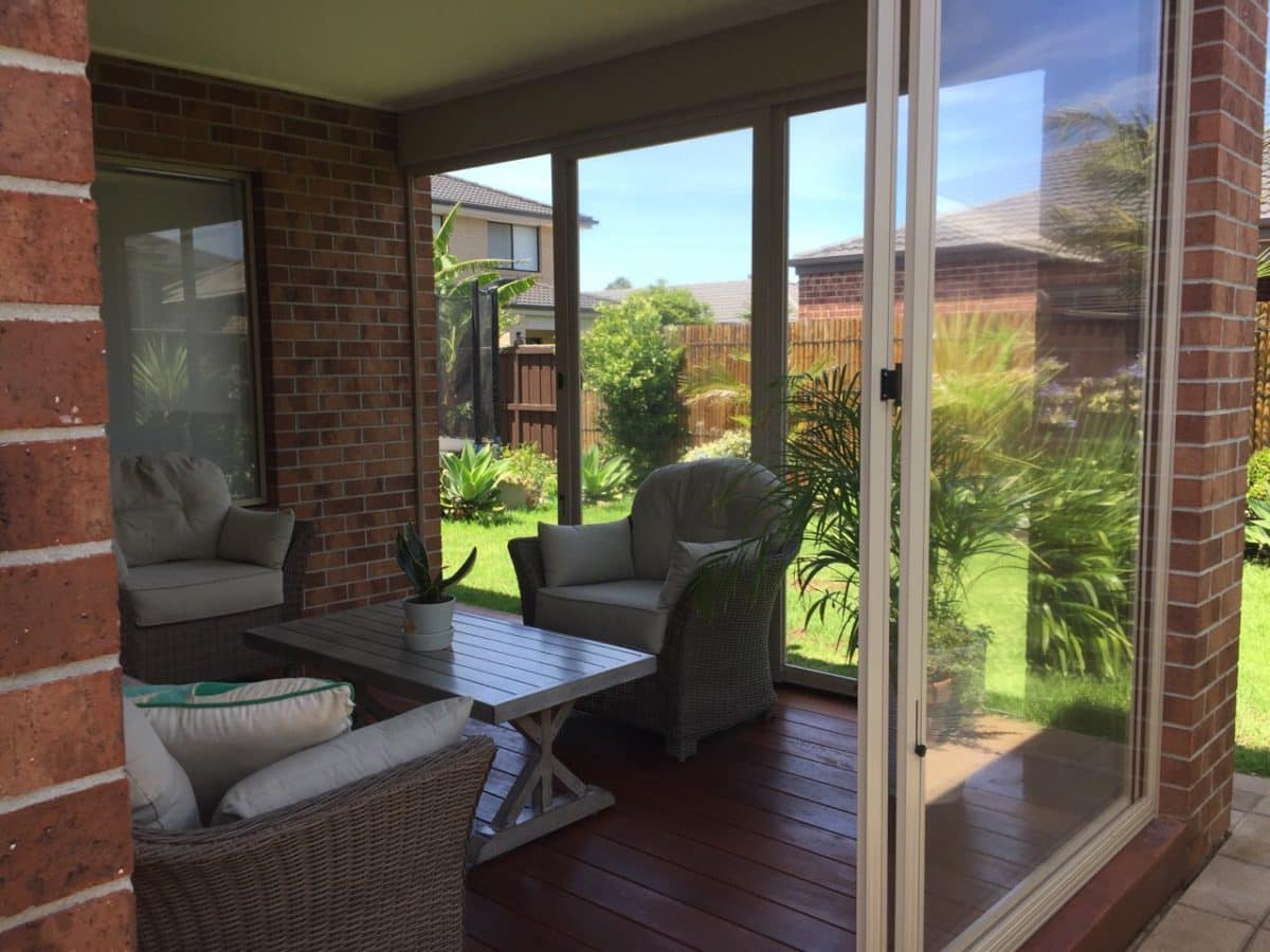 Bright, open outdoor living room with weather screens rolled back to the garden